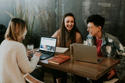 Three people at a table laughing and using their laptops